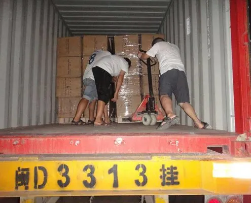 Workers loading packaged cartons into a shipping container