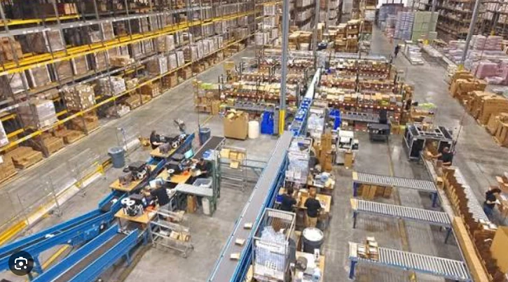 Elevated view of a factory packing area with conveyor lines, worktables, shelving and cartons